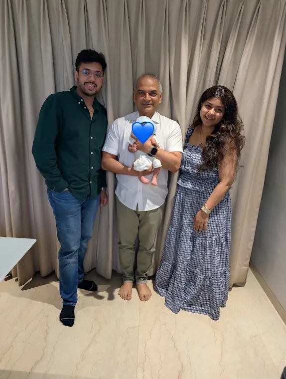 Dr. Patani holding a newborn with the baby's parents; the baby's face is covered with a heart