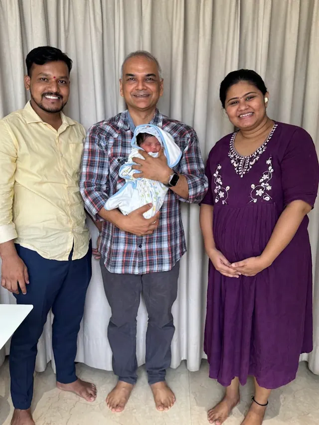 Dr. Patani holding a newborn, standing with the baby's parents
